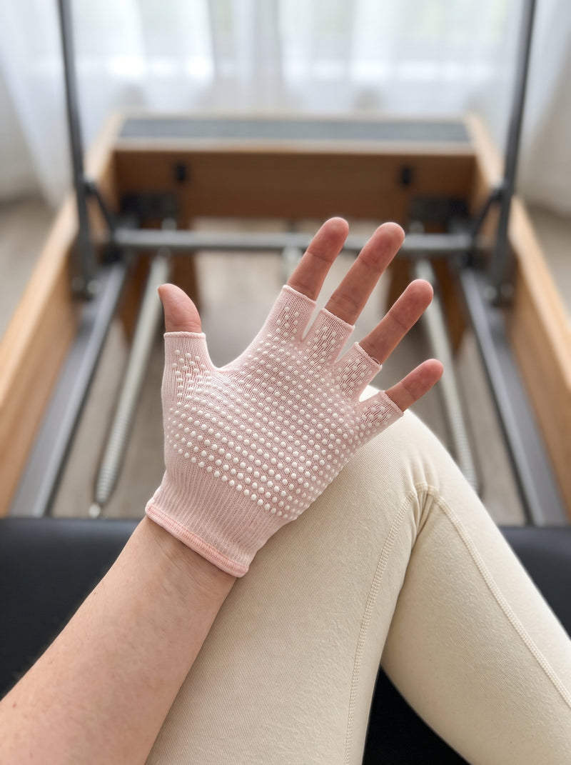 Open palm of a rosé pink SoftGrip glove resting on a knee at a reformer, raised white grip dots across the palm