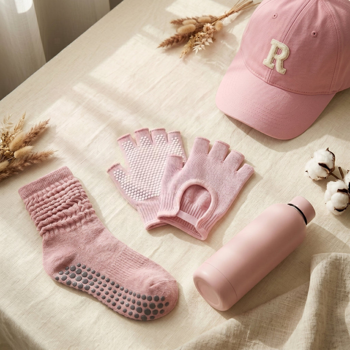 Rosé SoftGrip Pilates gloves with a pink Scrunch sock, the RKKN cap and a SoftSip bottle on cream linen
